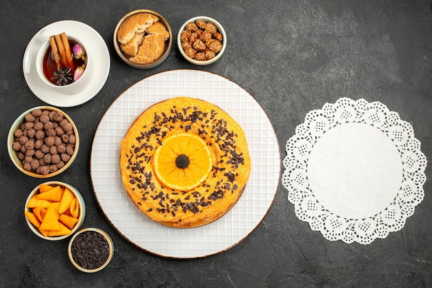 Вид сверху вкусный сладкий пирог с дольками апельсина и чашкой чая на темном столе печенья пирог бисквитный торт десертный чай