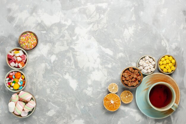 Top view of delicious sweetness composition candies and marshmallow with cup of tea on white surface