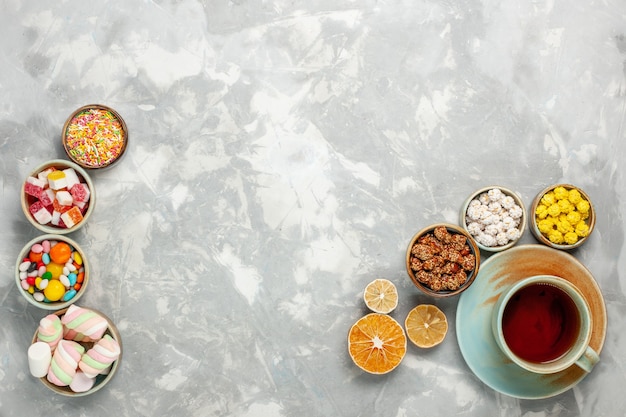 Вид сверху на вкусные сладкие композиции из конфет и зефира с чашкой чая на белой поверхности