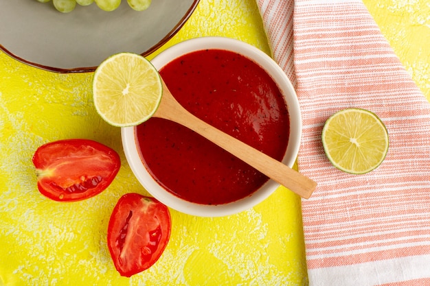 Вид сверху вкусный томатный соус с лимоном и помидорами на желтом столе, суп, еда, ужин