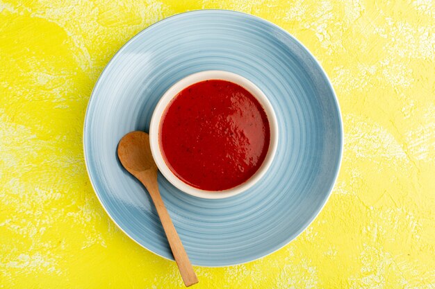 Top view delicious tomato soup inside blue plate on yellow table, soup food meal dinner