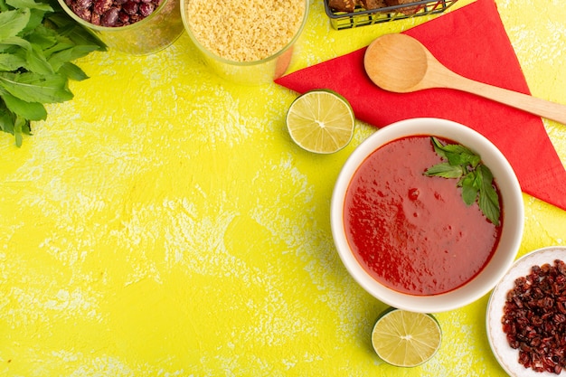 Вид сверху вкусный томатный суп с буханками хлеба с лимоном на желтом столе, суп из овощей на ужин