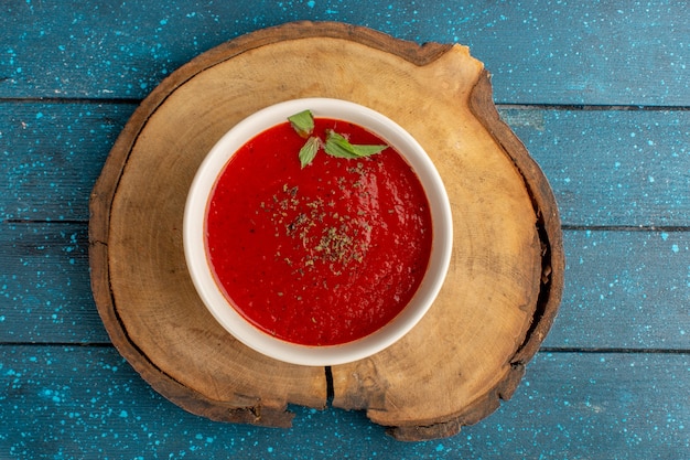 Вид сверху вкусного томатного супа с приправами внутри на синем столе, суп из овощей на ужин