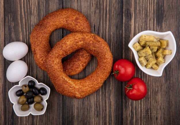 Top view of delicious turkish sesame bagels with olives on a bowl with tomatoes and eggs isolated on a wooden background