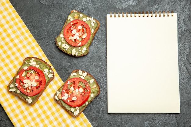 Foto gratuita vista dall'alto deliziosi panini utili con pasta di avocado e pomodori sullo spuntino del panino del pane dell'hamburger del panino della scrivania grigia