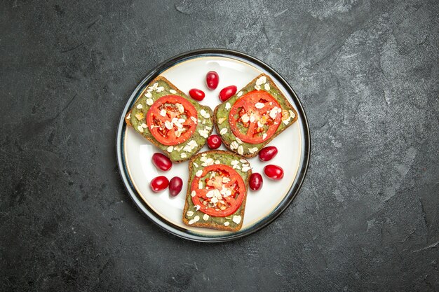 Вид сверху вкусные полезные бутерброды с пастой из авокадо и помидорами внутри тарелки на сером фоне, бутерброд с гамбургером, закуска из хлебной булочки