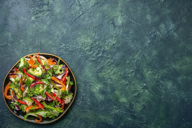 暗い背景の右側にさまざまな新鮮な野菜が入ったプレートのおいしいビーガンサラダの上面図