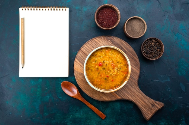 Вид сверху вкусный овощной суп внутри круглой тарелки с приправами на темно-синем столе.