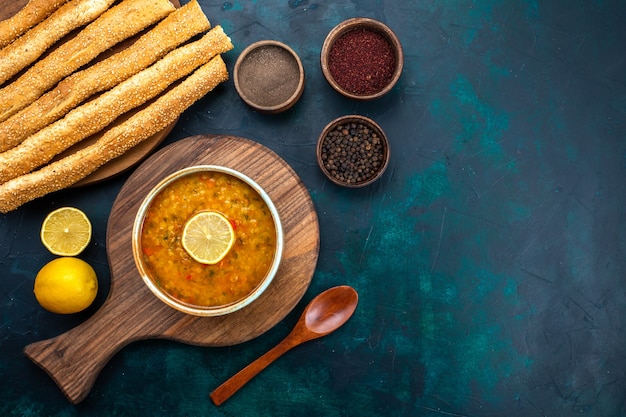 Foto gratuita vista dall'alto una deliziosa zuppa di verdure all'interno del piatto rotondo con condimenti limone e pane sulla scrivania blu scuro.