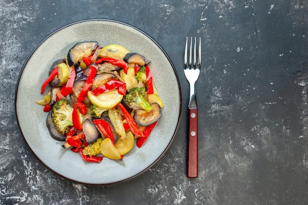 Free photo top view of delicious vegetarian meal on a plate and fork on the right side on dark background