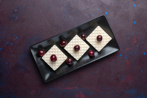 Top view of delicious waffles with cherries inside plate on dark surface