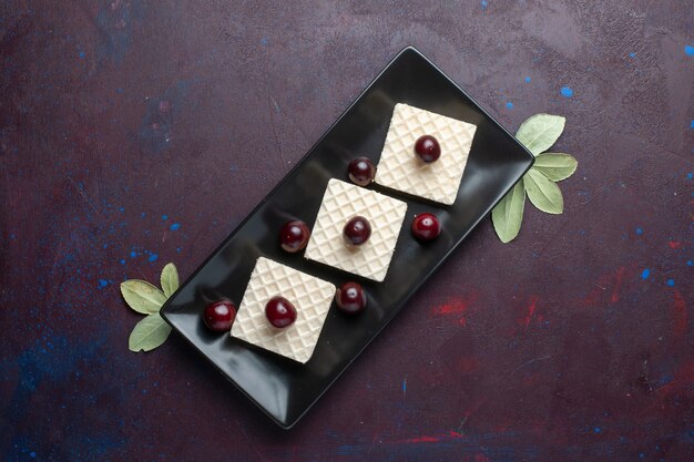 Top view of delicious waffles with cherries inside plate on the dark surface