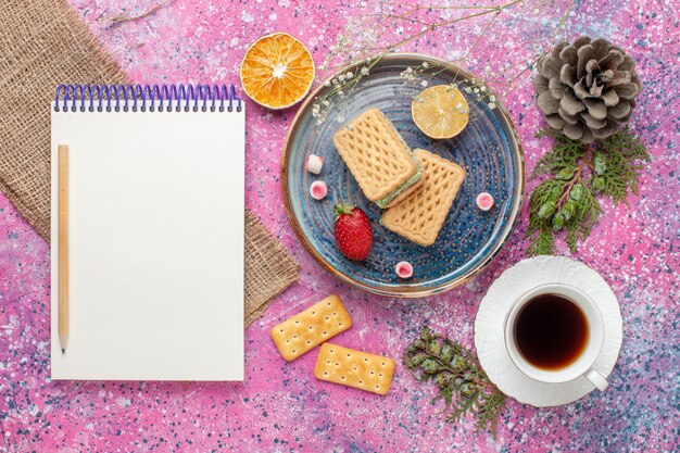 Top view of delicious waffles with cup of tea on pink surface