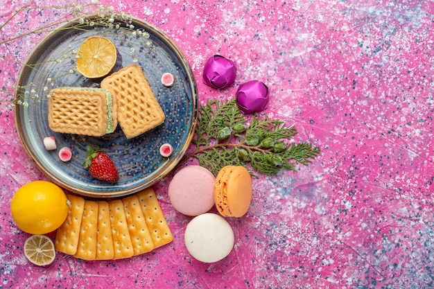 Vista dall'alto di deliziosi waffle con macarons francesi e cracker sulla superficie rosa