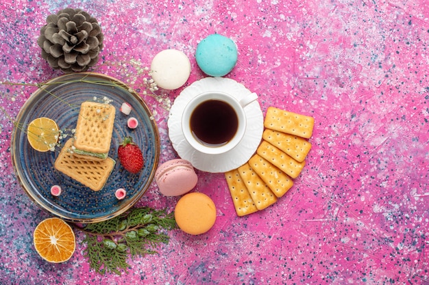 Top view of delicious waffles with french macarons crackers and tea on pink surface