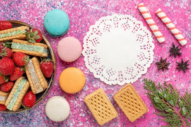 Vista dall'alto di deliziosi waffle con macarons francesi e marshmallow sulla superficie rosa