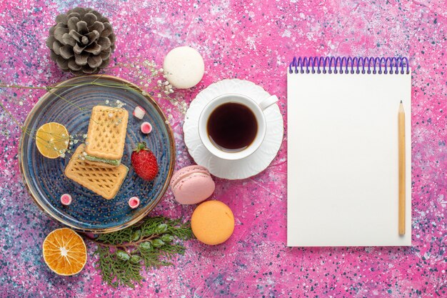 Vista dall'alto di deliziosi waffle con macarons francesi e tè sulla superficie rosa