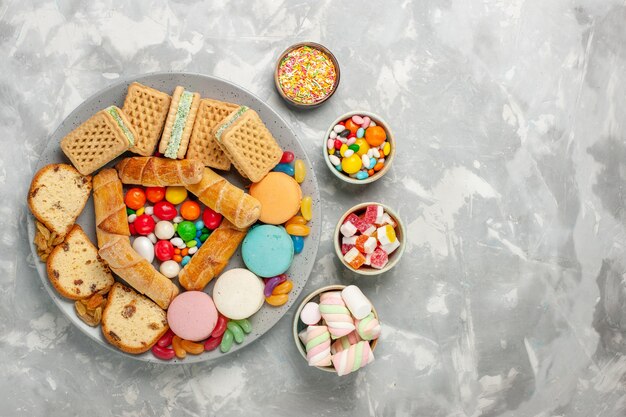Top view of delicious waffles with macarons cake slices and candies on light white surface