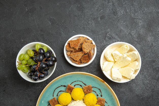 Top view delicious yellow candies with cake grapes and cheese on dark grey background sugar fruit candy tea cake sweet