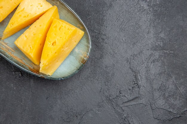 Top view of delicious yellow sliced chees on a blue plate on the right side on black background