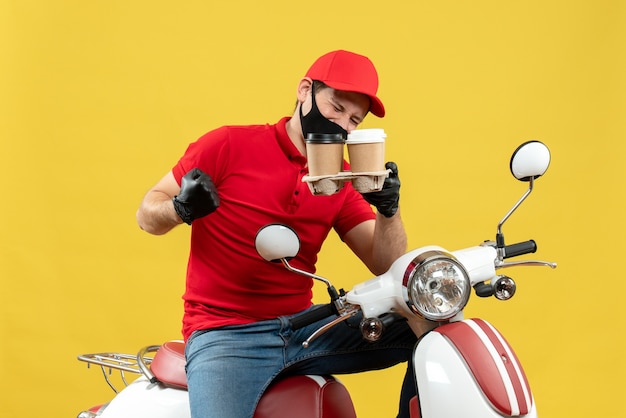 Top view of delivery guy wearing uniform and hat gloves in medical mask sitting on scooter showing orders feeling proud