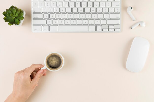 Top view of desk with keyboard and hand holding coffee cup