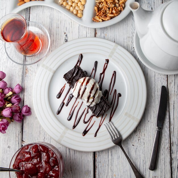 Top view dessert in plate with tea, nuts, fruit jam, flowers on white wooden background.