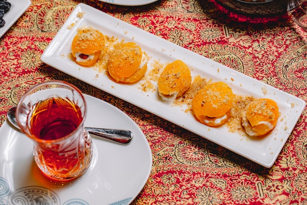 Top view dessert sweet peaches with nuts and cream and a glass of tea