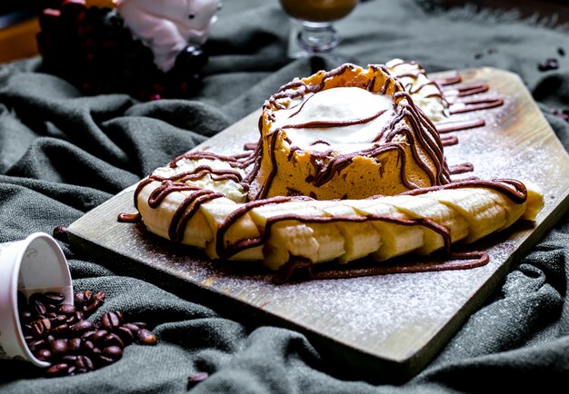 Top view dessert with ice cream and whipped cream garnished with sliced Ã¢ÂÂÃ¢ÂÂbanana and poured chocolate on the board