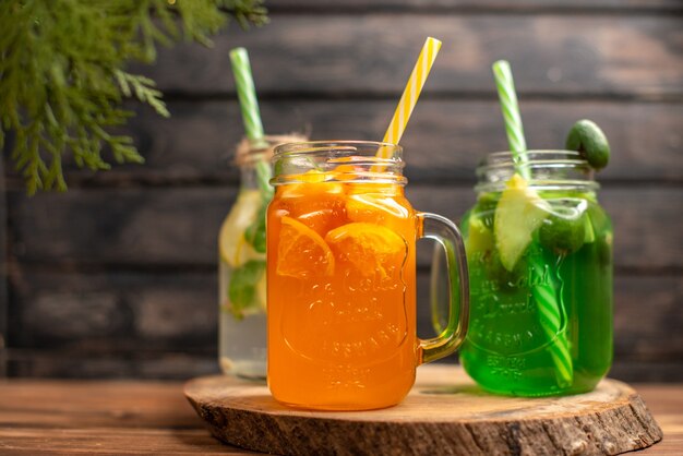 Top view of detox water and fresh juice in bottles with tubes on the left side on brown wooden background