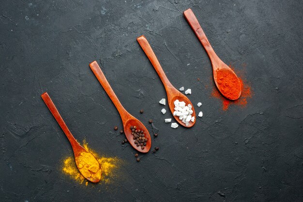 Top view diagonal row wooden spoons with turmeric black pepper sae salt red pepper powder on black table