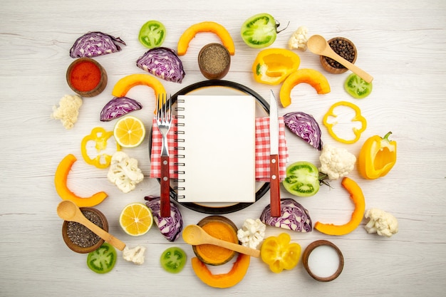 Top view diet written on notepad fork and knife on round plate cut vegetables different spices in bowls on wooden table