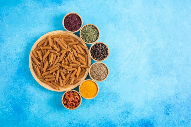 Top view of dietic pasta on wooden board and various kinds of spices over blue background.