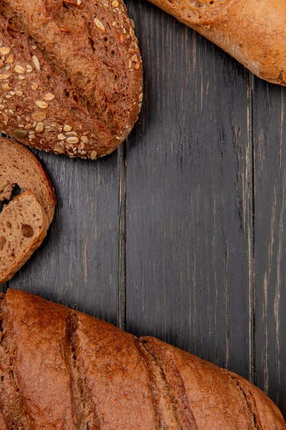 Top view of different breads as rye black baguette on wooden background