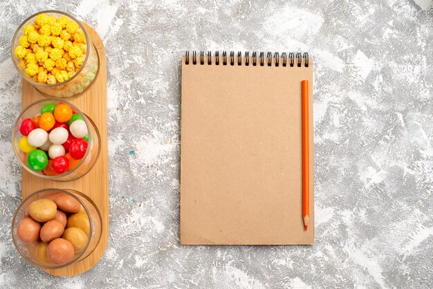 Top view of different candies colorful sweets with notepad on white surface