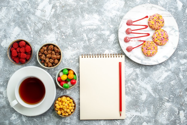 Top view different candies with nuts biscuits and cup of tea on white space