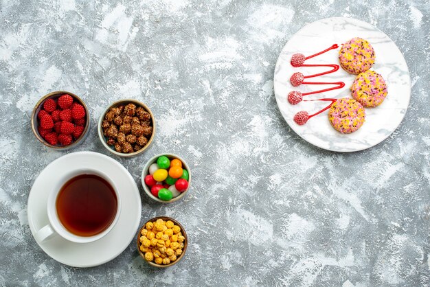 Top view different candies with nuts and cup of tea on a white space