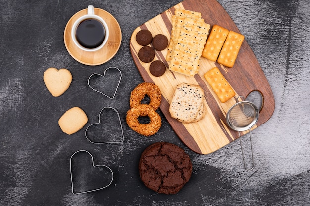 Top view different cookies and coffee cup on dark surface