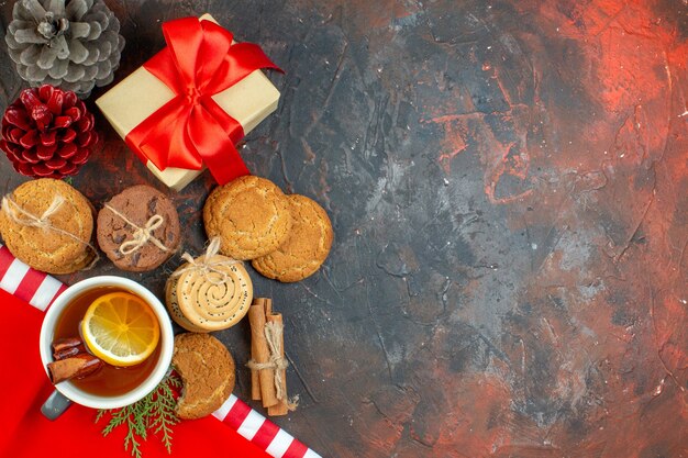 Top view different cookies tied with rope cup of tea pinecones cinnamon sticks on dark red table with copy place