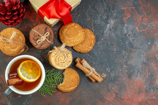 Top view different cookies tied with rope cup of tea pinecones gift on dark red table with free space