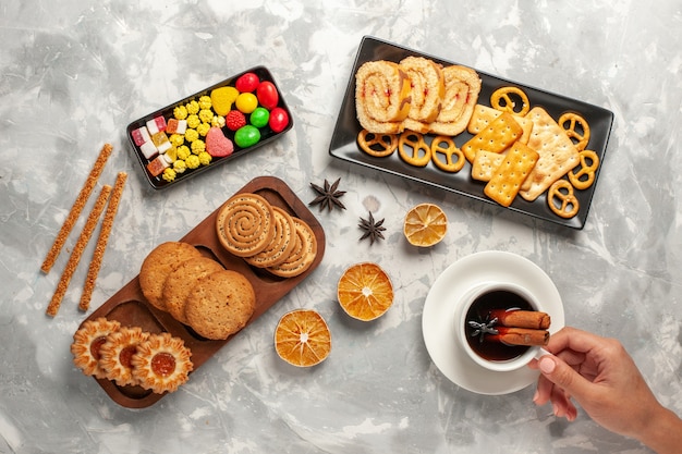 Top view different cookies with candies and cup of tea on white desk cookie biscuit sugar bake cake sweet pie