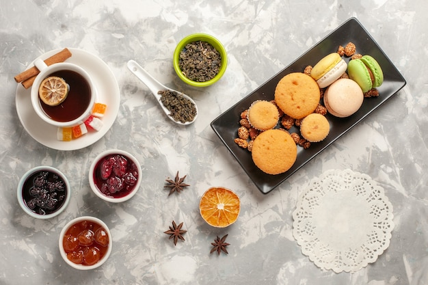 Top view different cookies with jams and cup of tea on the white desk biscuit sugar pie cake sweet cookies