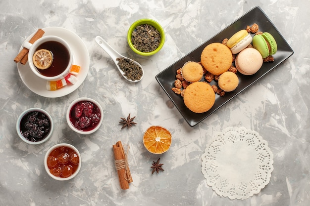 Top view different cookies with jams and cup of tea on the white surface biscuit sugar pie cake sweet cookies