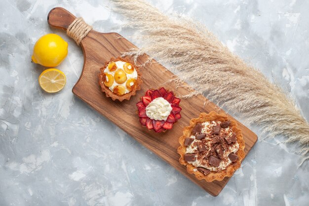 上面図さまざまなクリーミーなケーキフルーティーなケーキとレモンの白い机の上のケーキ焼きビスケット甘い砂糖の果実