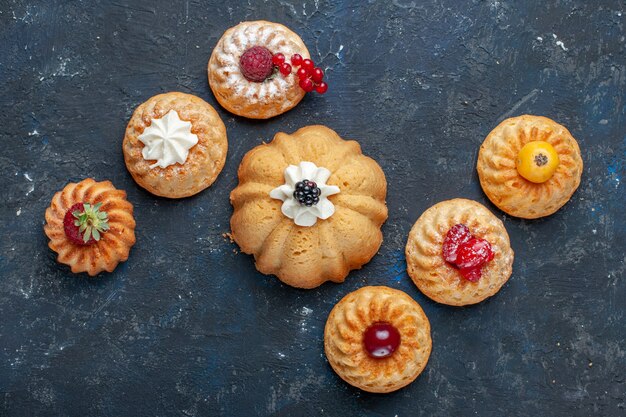 Top view of different delicious cakes baked with cream and berries on dark, berry fruit bake cake biscuit sweet