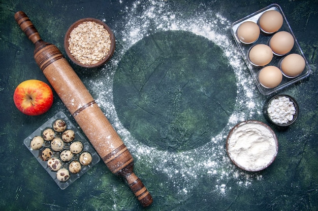 Foto gratuita vista dall'alto diversi ingredienti dell'impasto farina bianca cereali e uova su superficie blu scuro