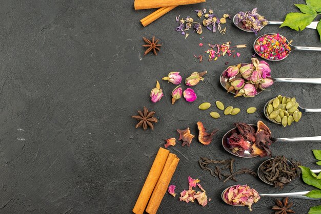 Top view different dried flavors on silver spoons with cinnamon on a dark gray surface