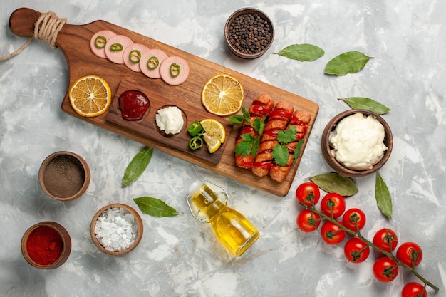 Vista dall'alto diversa composizione alimentare salsicce con pomodori freschi condimenti olio e limoni su luce scrivania pasto cibo veegtable foto a colori