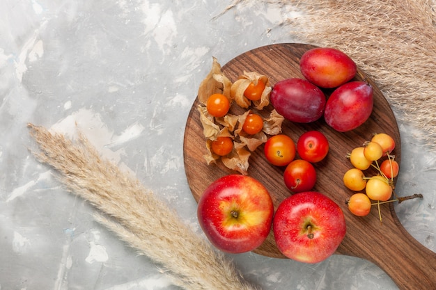 Вид сверху различные сформированные сливы кислые и свежие фрукты с яблоками на светлом белом столе.