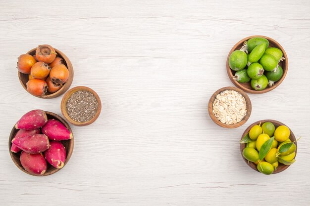 Вид сверху различных свежих фруктов внутри тарелок на белом фоне тропических спелых экзотических здоровых цветов диеты